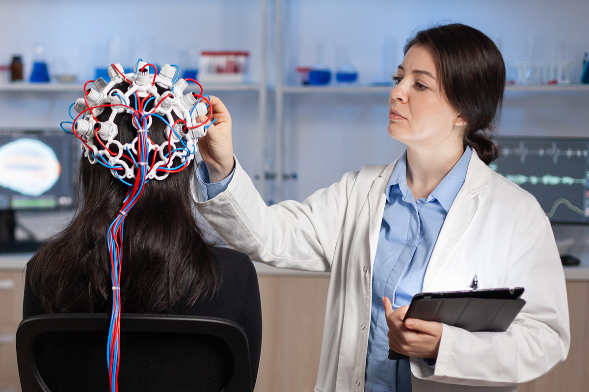 Doctor in white coat attaches electrodes to the head of a patient in a lab.