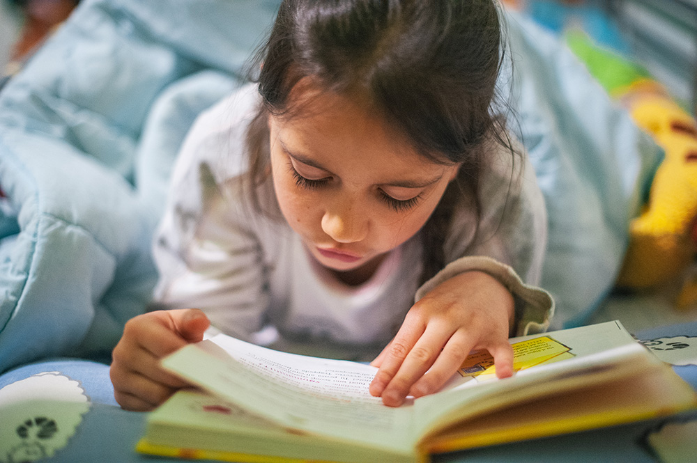 Young girl reads a book while lying on her stomach