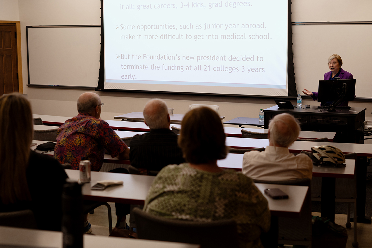 Diana Zuckerman speaks to a crowd in a lecture hall while a presentation shows on the projector screen beside her.