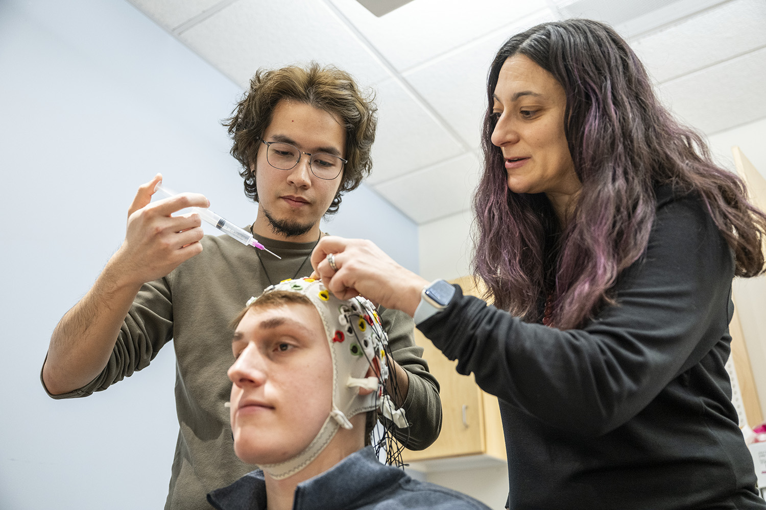 Two researchers lean over a seated person wearing an EEG cap