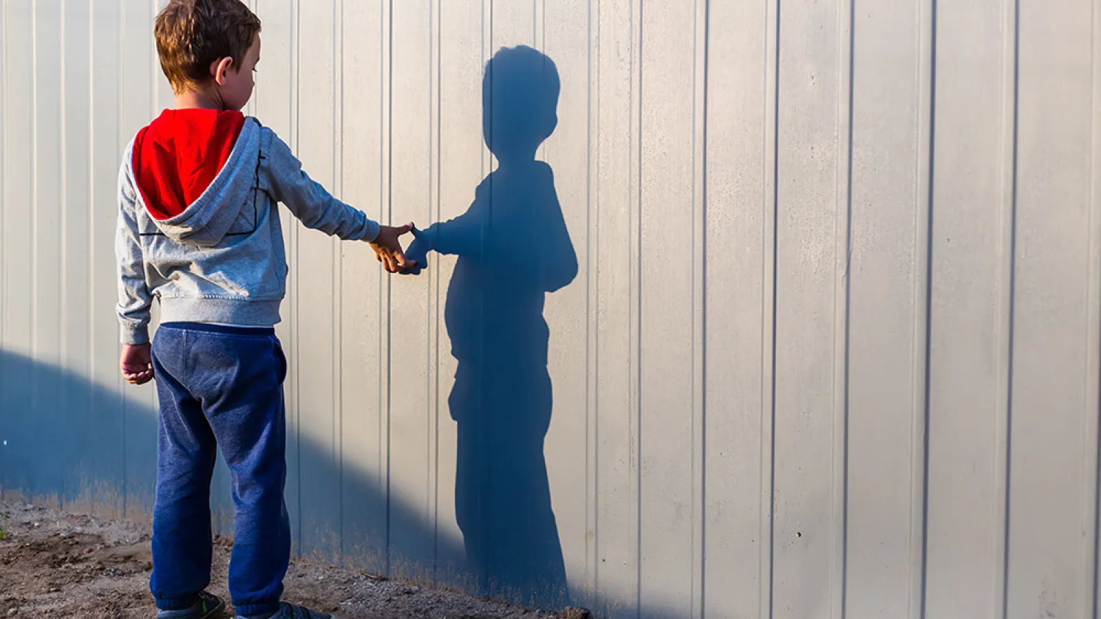 A child reaches out to touch his shadow on a white wall
