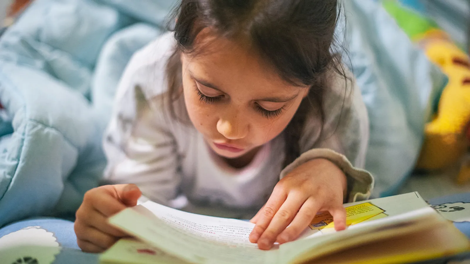 Young girl reads a book while lying on her stomach