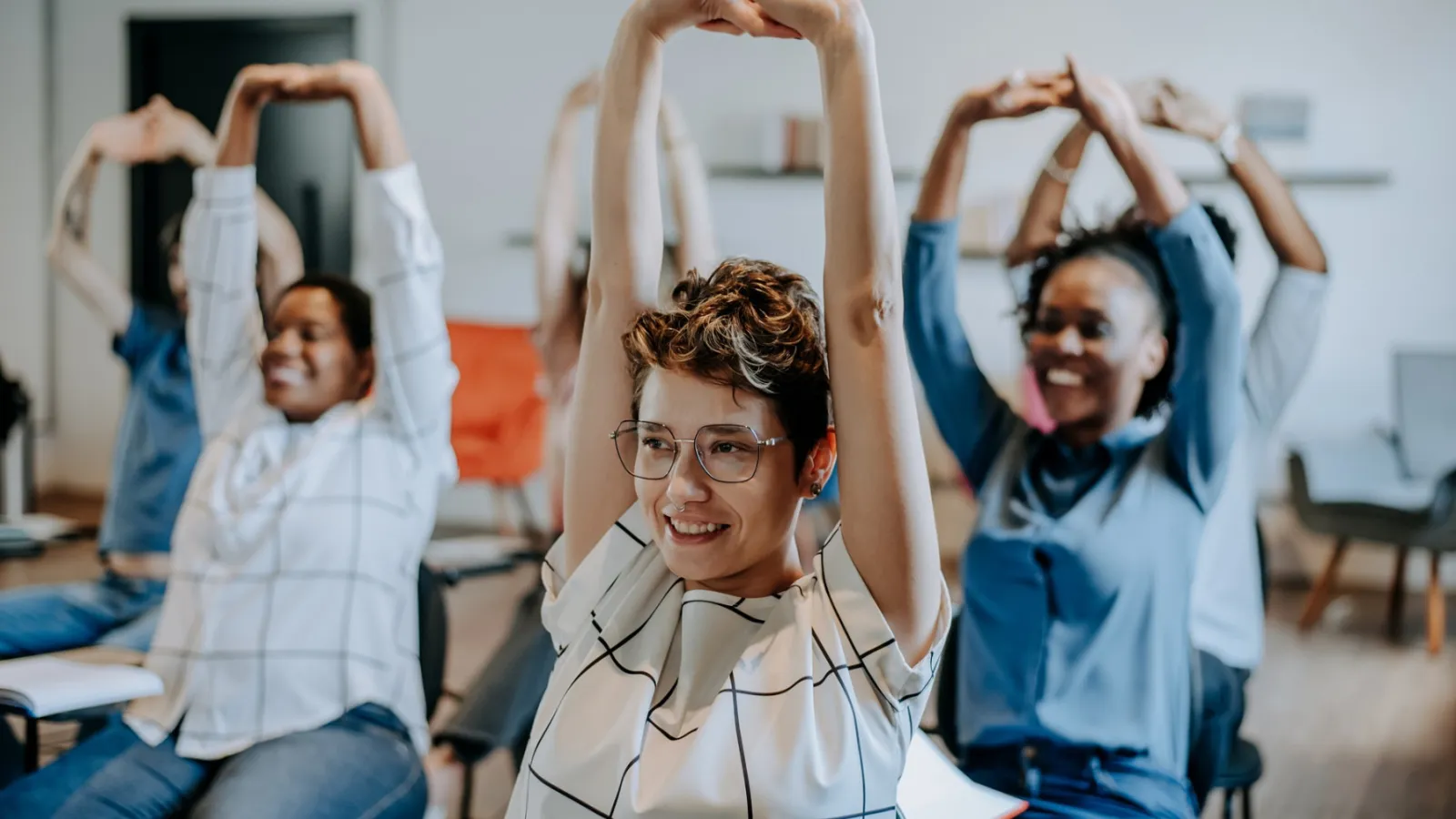 Students stretch their arms above their heads while sitting at desks.