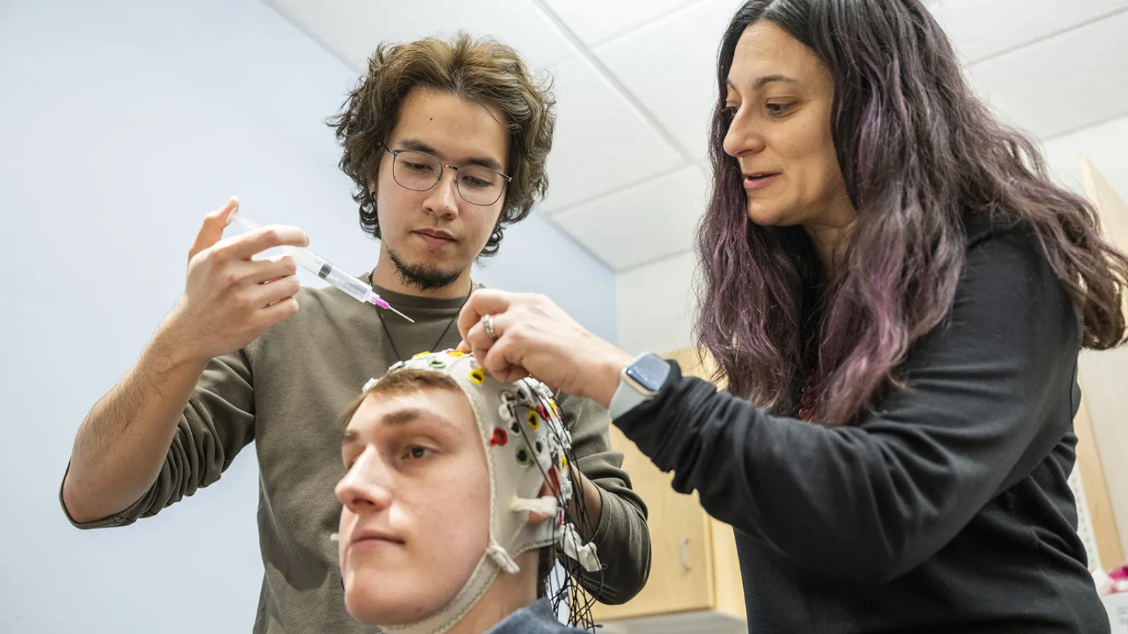 Two researchers lean over a seated person wearing an EEG cap