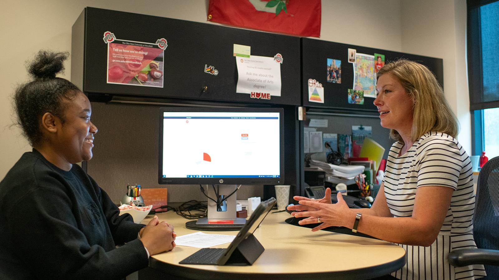 An advisor and student sit at a desk and talk
