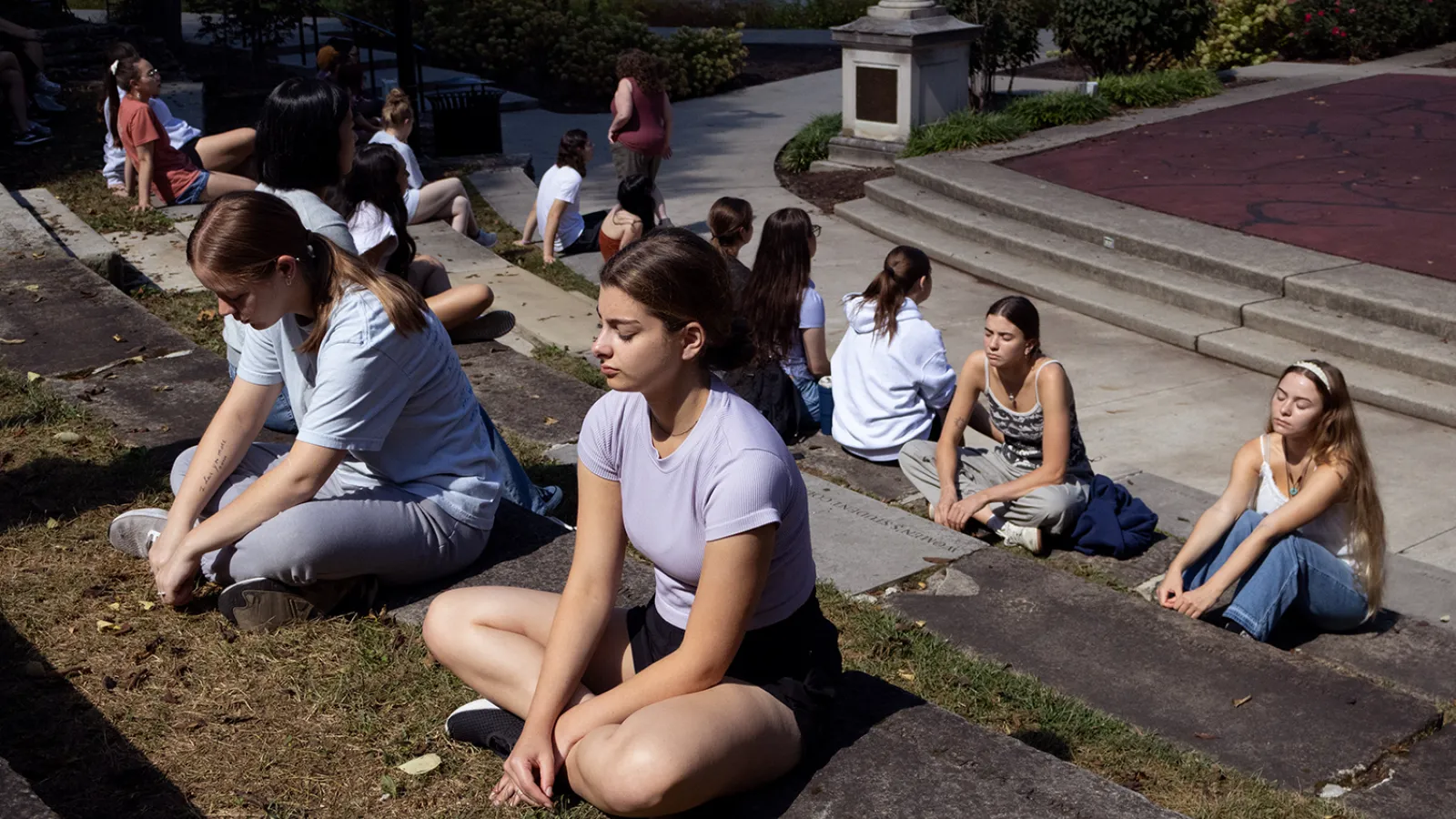 Students sit in rows in an outdoor amphitheater with their eyes closed