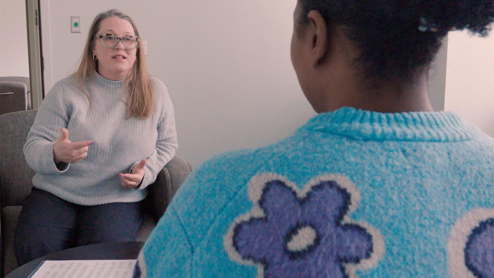 A therapist speaks to a client as the two of them sit opposite each other in a room