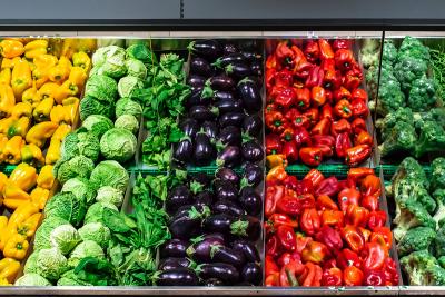 Grocery store produce section, with rows of yellow peppers, cabbage, eggplant, and broccoli.