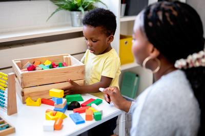 A child plays with multi-colored blocks as an adult looks on.