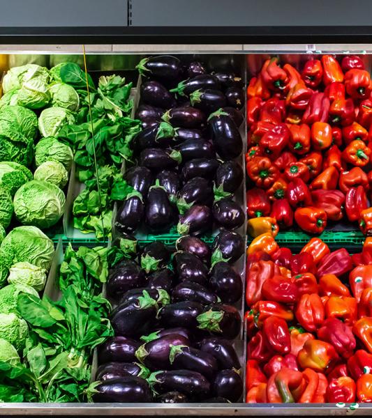 Grocery store produce section, with rows of yellow peppers, cabbage, eggplant, and broccoli.