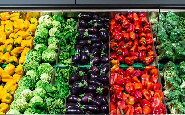 Grocery store produce section, with rows of yellow peppers, cabbage, eggplant, and broccoli.