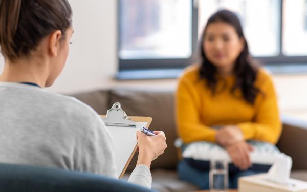 A therapist with a clipboard sits in an office with a patient.