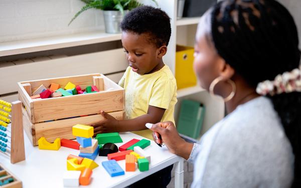A child plays with multi-colored blocks as an adult looks on.
