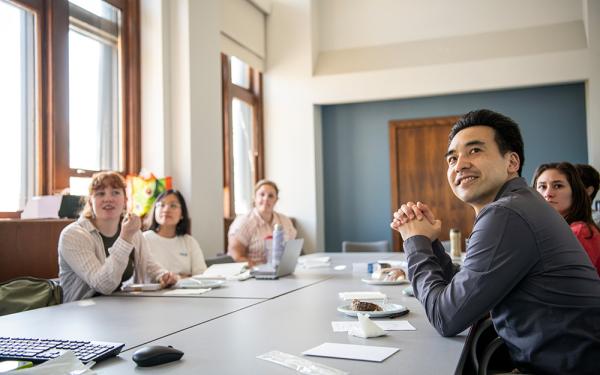 Professor Ken Fujita and students sitting around a classroom table during a slide presentation.