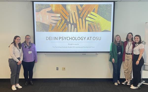 Students stand on either side of a projector screen during a conference.