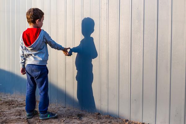 A child reaches out to touch his shadow on a white wall
