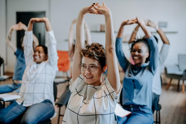 Students stretch their arms above their heads while sitting at desks.