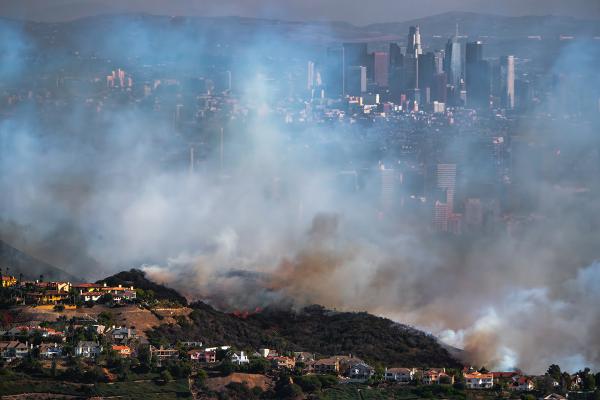 Wildfire smoke looms over a line of hilltop houses with the city of Los Angeles visible in the background