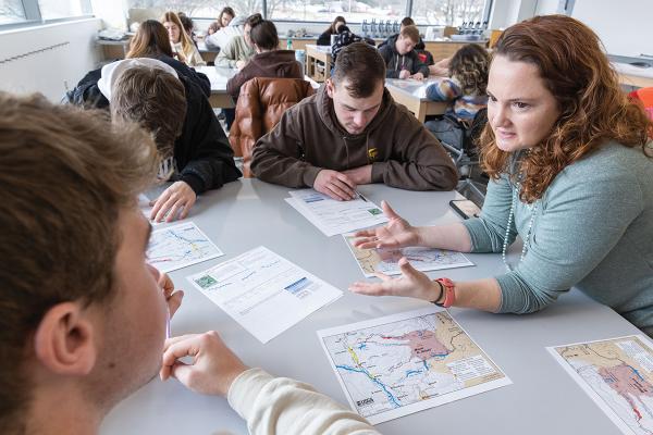 A professor works with a group of students at a table.