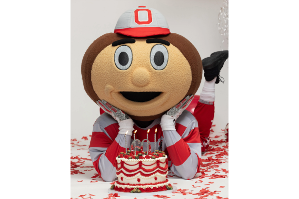 Brutus laying on his stomach with his hands on his chin, with a birthday cake placed in front of him. 
